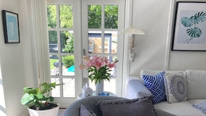 Ein Wohnzimmer mit einem grauen Sofa, einem weißen Sessel und einem Couchtisch. Auf dem Couchtisch steht eine Topfpflanze und eine Vase mit Blumen.