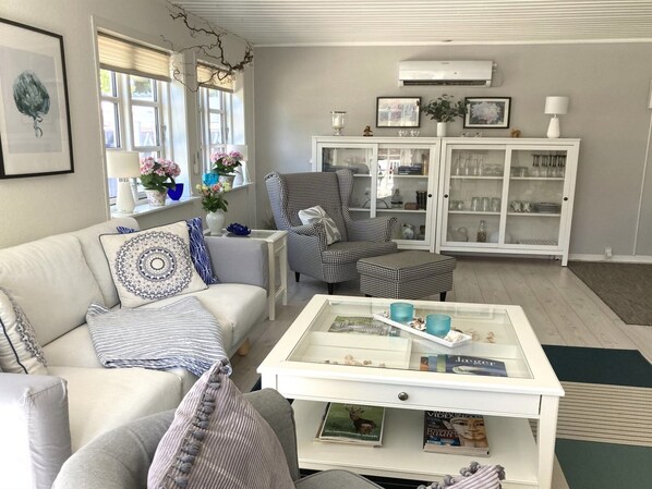 A living room with a white sofa, patterned armchairs, a coffee table with magazines, and a white cabinet with glass doors.