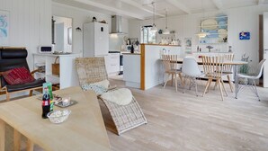 A spacious living area with a dining table, chairs, and a kitchen area with white cabinets and a wooden ceiling. - "Bernadeta" - 1.2km from the sea by Interhome (Blokhus)