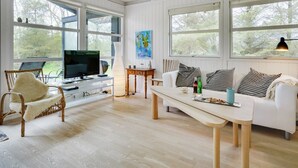 A spacious living room with a white sofa, a TV on a stand, a wooden table, and a large window offering a view of trees. - "Bernadeta" - 1.2km from the sea by Interhome (Blokhus)
