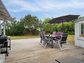 Een houten terras met een tafel, stoelen, een barbecue en een parasol.