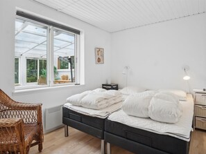 Een slaapkamer met een bed, een stoel, een nachtkastje, een lamp en een raam met uitzicht op groen.
