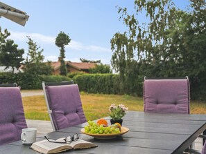 Een tafel met een boek, brillen, een schaal fruit en een kop.
