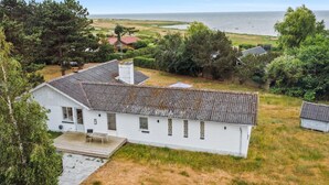 Een wit huis met een pannendak, omringd door groen en met uitzicht op zee.