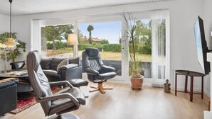 Een moderne woonkamer met een bank, twee stoelen, een televisie en een groot raam met uitzicht op groen.
