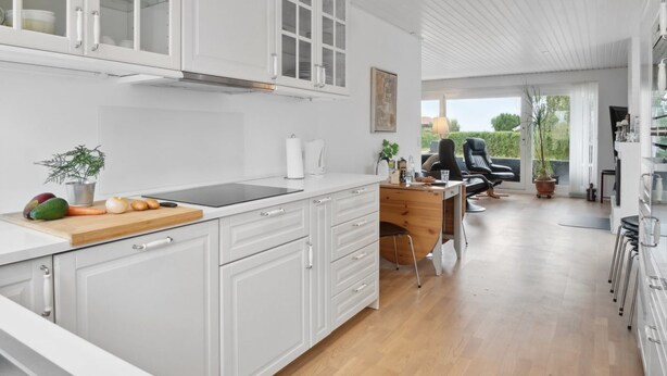 Een moderne keuken met witte kasten, een centraal eiland met een snijplank en een eethoek met een stoel en tafel.