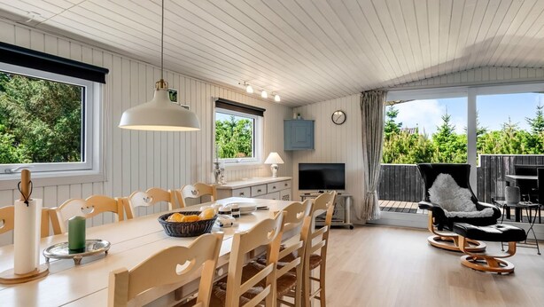 Un comedor amplio con una larga mesa y sillas, un televisor y vistas al exterior.