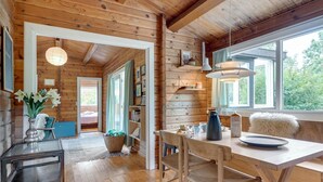 A wooden cabin interior with a dining area, a kitchen, and a bedroom visible through an open door.