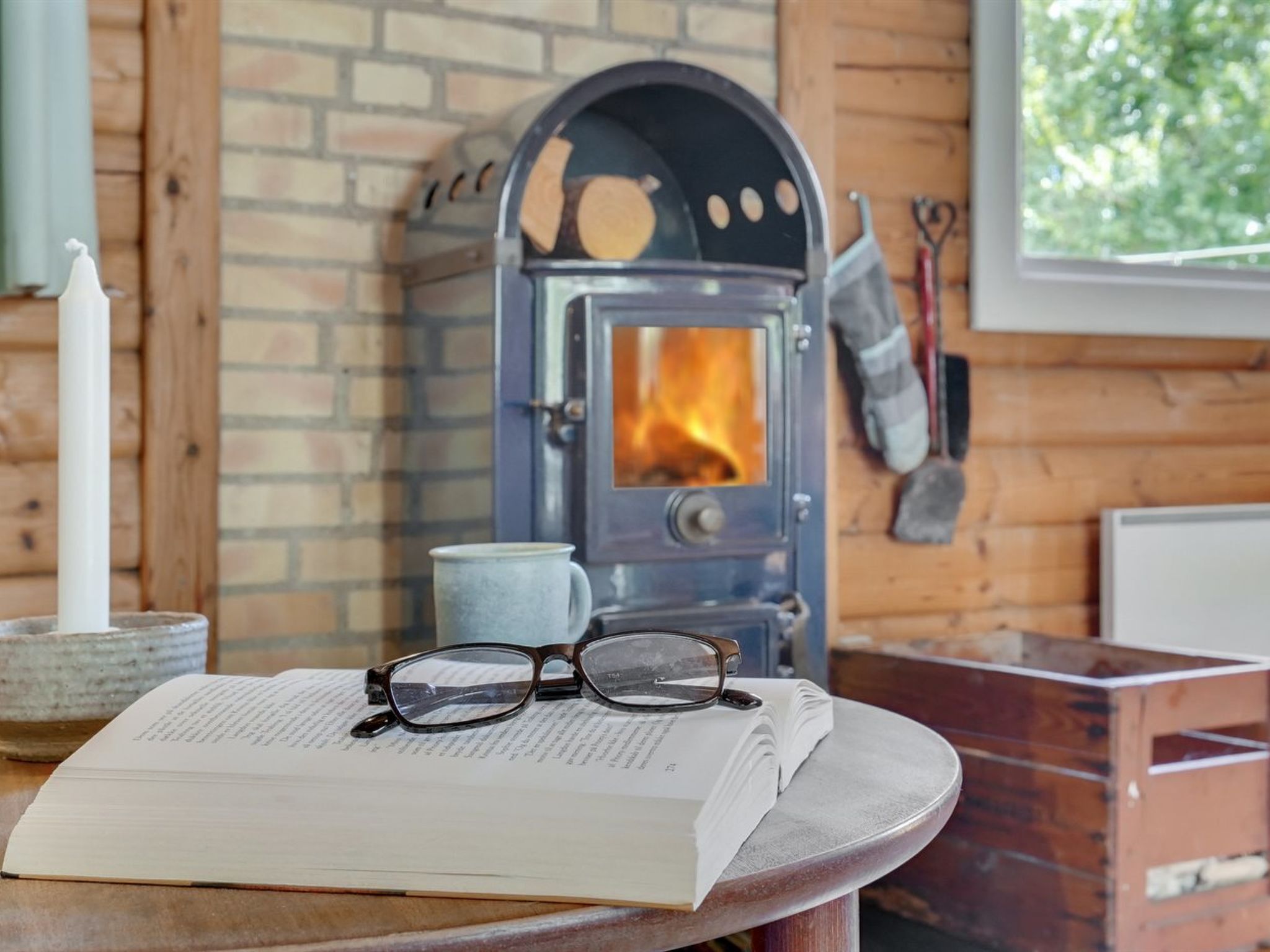 Een knus vertrek met een houtkachel, een boek en brillen op een tafel.