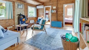 A cozy cabin interior with a fireplace, a sofa, a chair, and a dining area.