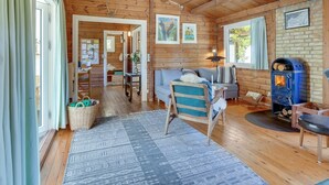 A cozy cabin interior with a wooden ceiling, a blue sofa, a small table, a blue wood-burning stove, and a patterned rug.
