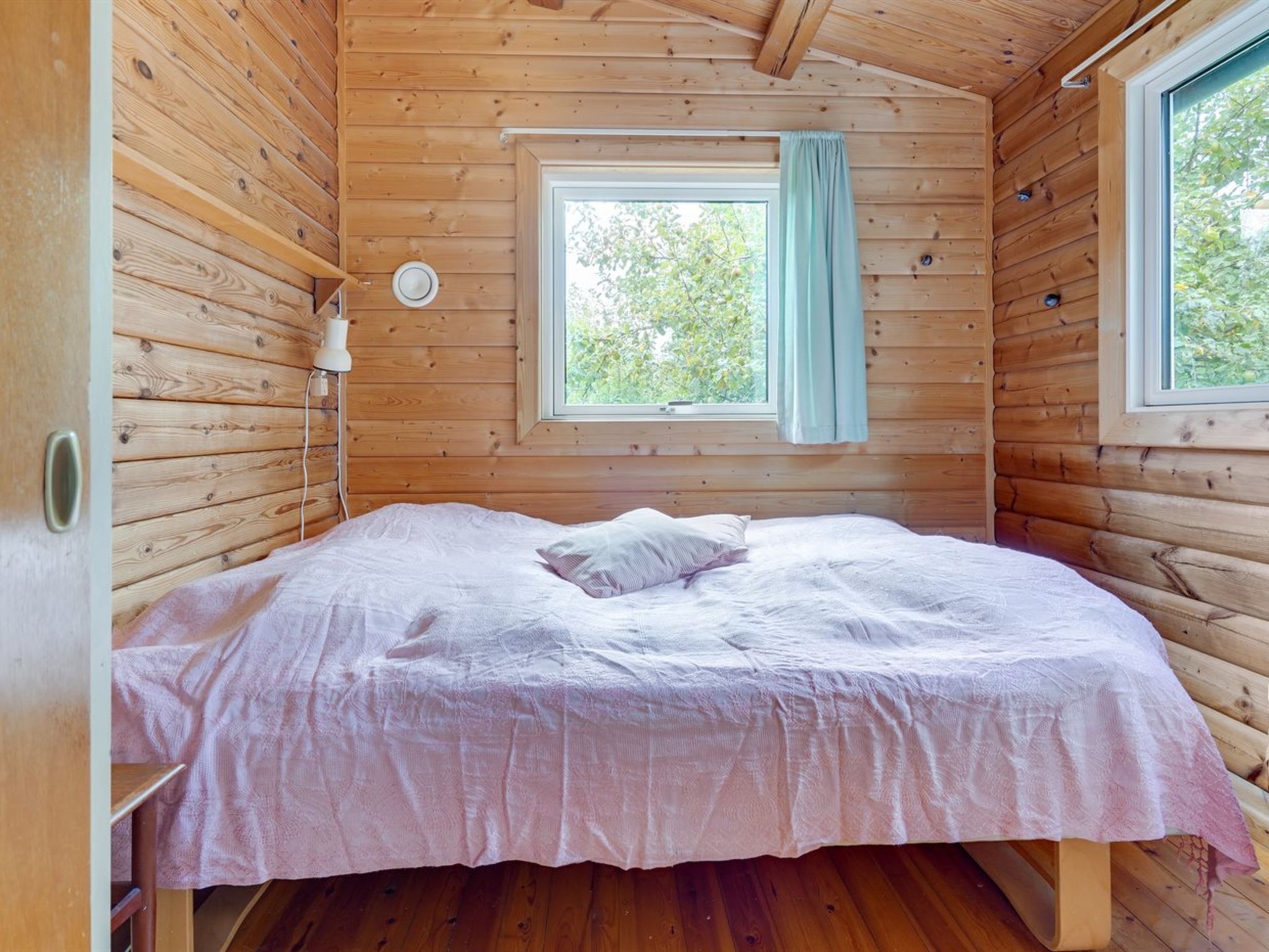 A wooden cabin bedroom with a bed, a window with a curtain, and a nightlight.