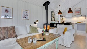 Un salon chaleureux avec un canapé blanc, une table basse en bois et une cuisine en arrière-plan.