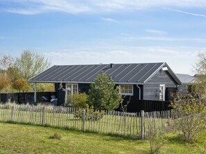 Une maison moderne avec une façade sombre, un toit en pente et une cour clôturée.