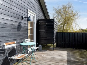 Une terrasse en bois avec une table et des chaises, une fenêtre et une clôture noire.