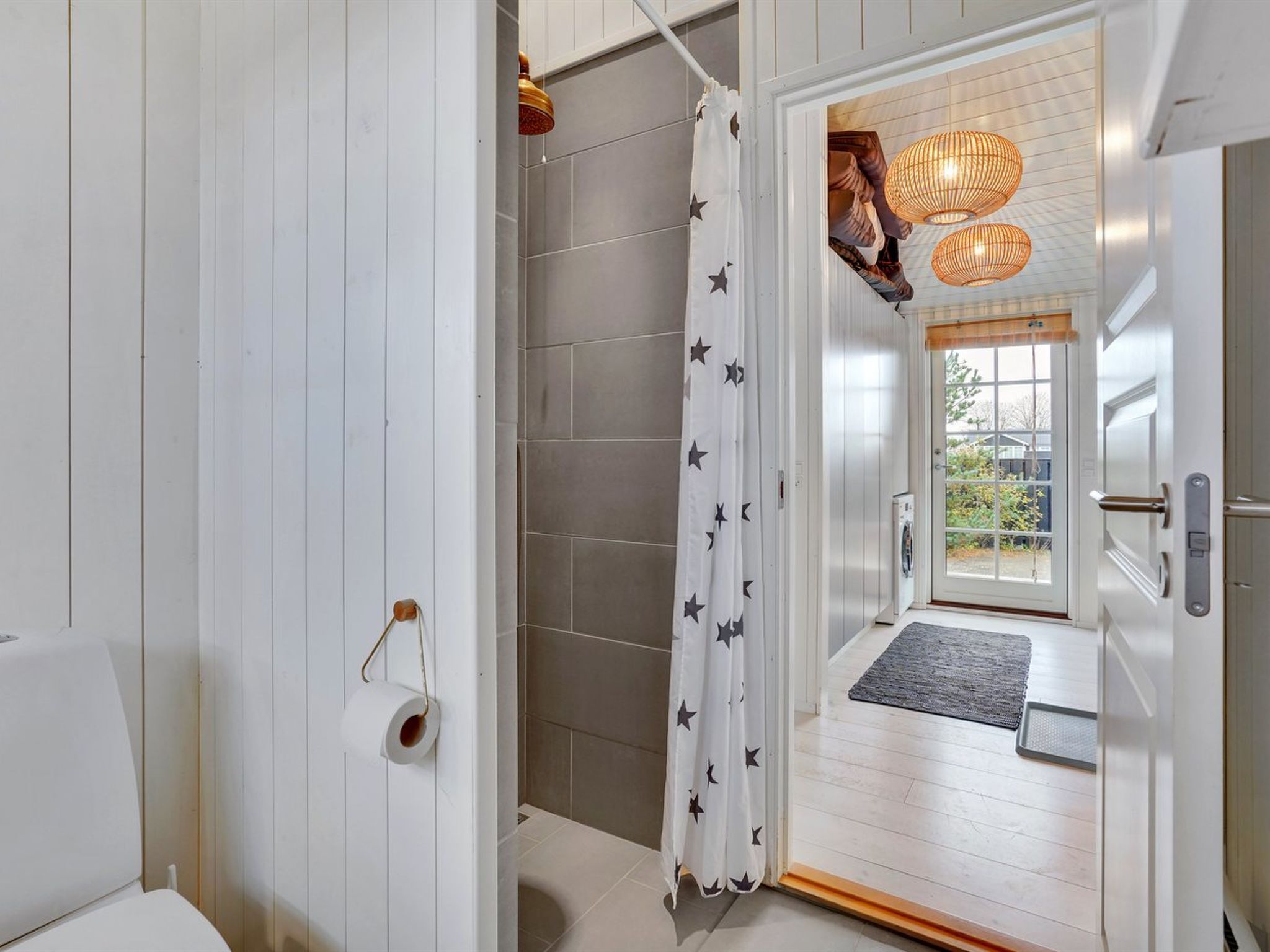 Uma casa de banho moderna com chuveiro, sanita e porta que dá para uma sala com vista.