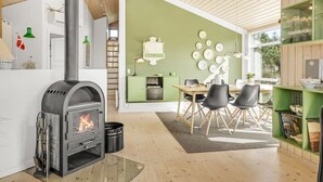 Una cocina moderna con estufa de leña, un área de comedor con pared verde y un mueble verde con cristalería.