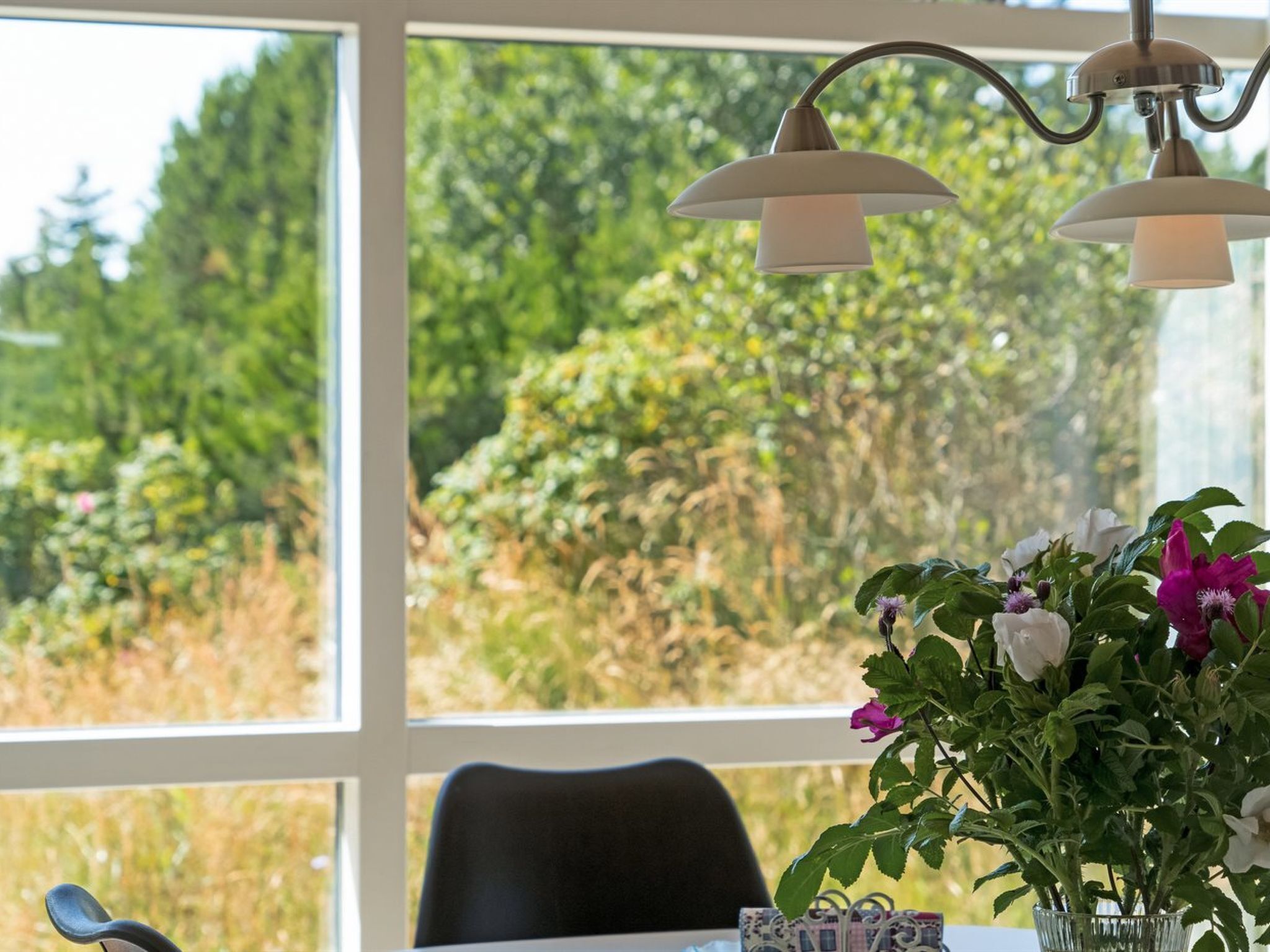 Une pièce avec une grande fenêtre, une table ornée d’un vase de fleurs et une chaise.