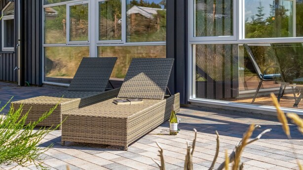 Un área de estar al aire libre y moderna con mobiliario de mimbre y una botella de vino, con vistas a un paisaje pintoresco.