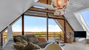 Um quarto moderno no estilo loft, com uma janela grande, um sofá, um abajur e uma televisão de tela plana.