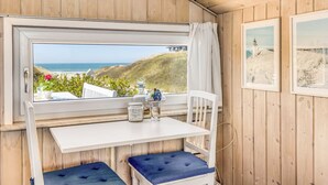A room with a wooden interior, a window with a view of the sea, a white table, a blue cushioned bench, and a clock on the wall. - "Doritea" - 50m from the sea by Interhome (Løkken)