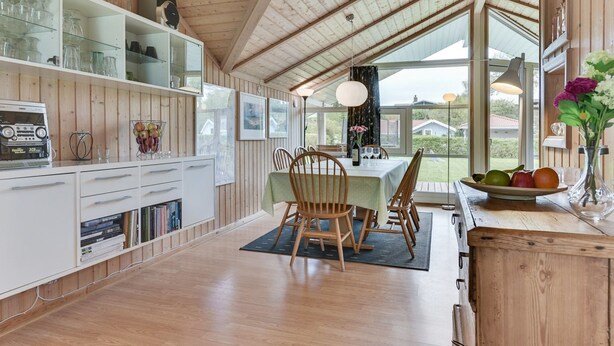 Un interior de madera con comedor, armarios blancos y un amplio ventanal con vistas al exterior.