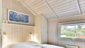 Un dormitorio con una cama, un ventanal con vistas a la vegetación y un cuadro en la pared.