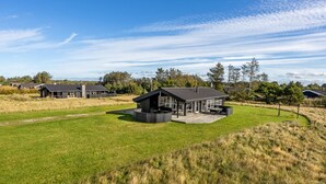 Een modern huis met een ruim terras, omgeven door een grasveld en bomen.