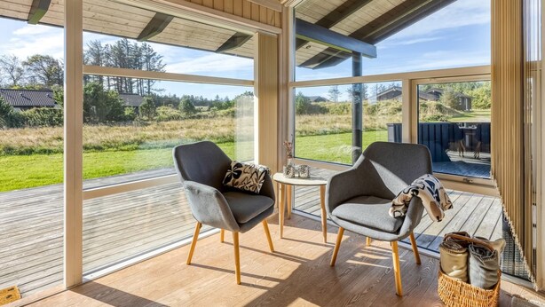Een ruime kamer met grote ramen, houten vloeren en twee grijze gestoffeerde stoelen.