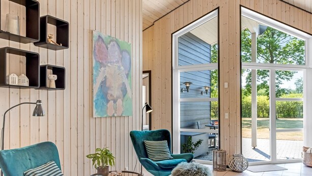 Een moderne woonkamer met smaragdgroene fauteuils, een groot abstract schilderij en uitzicht op de omgeving.