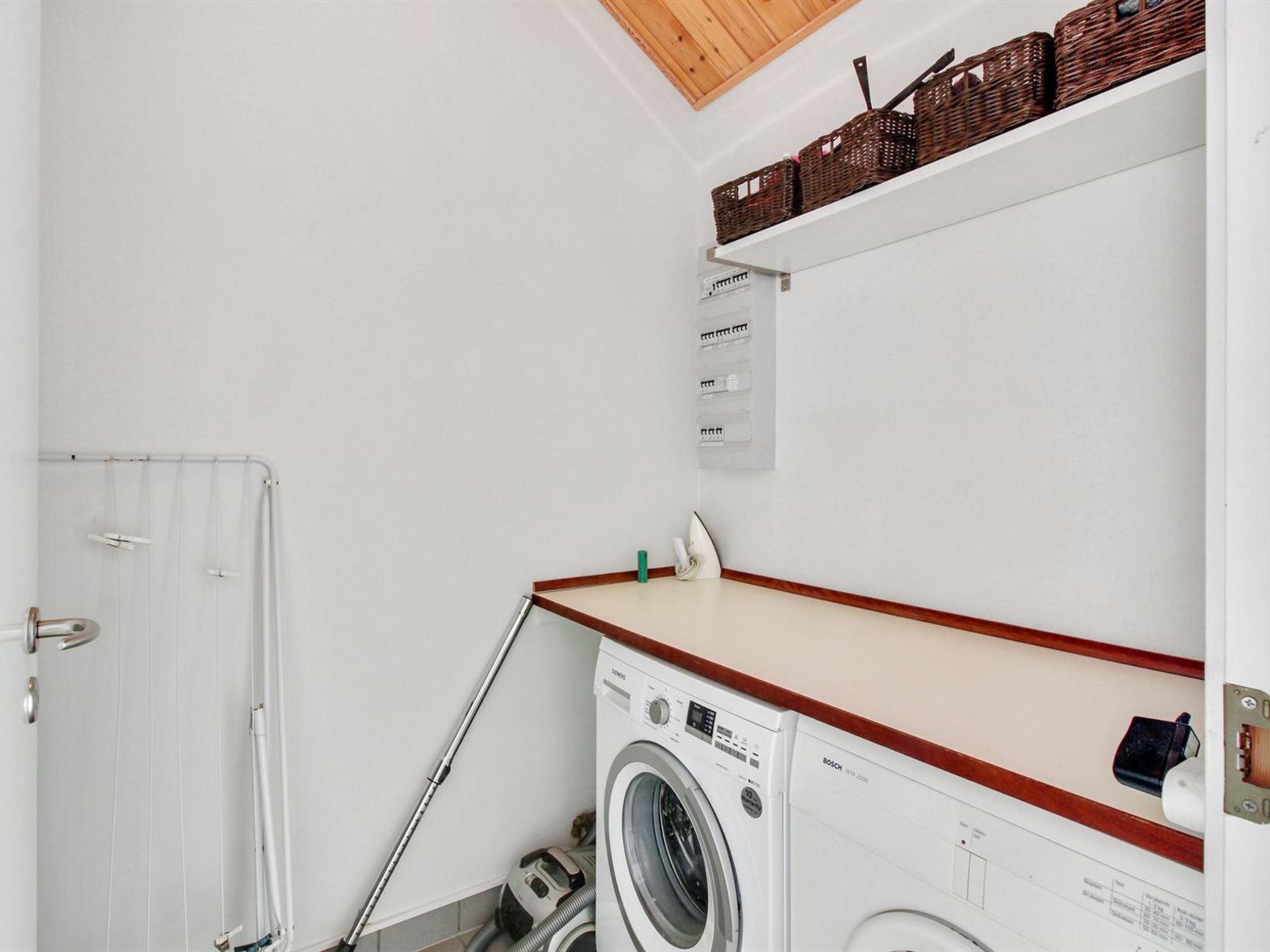 A laundry room with a washing machine, a drying rack, and a white door.