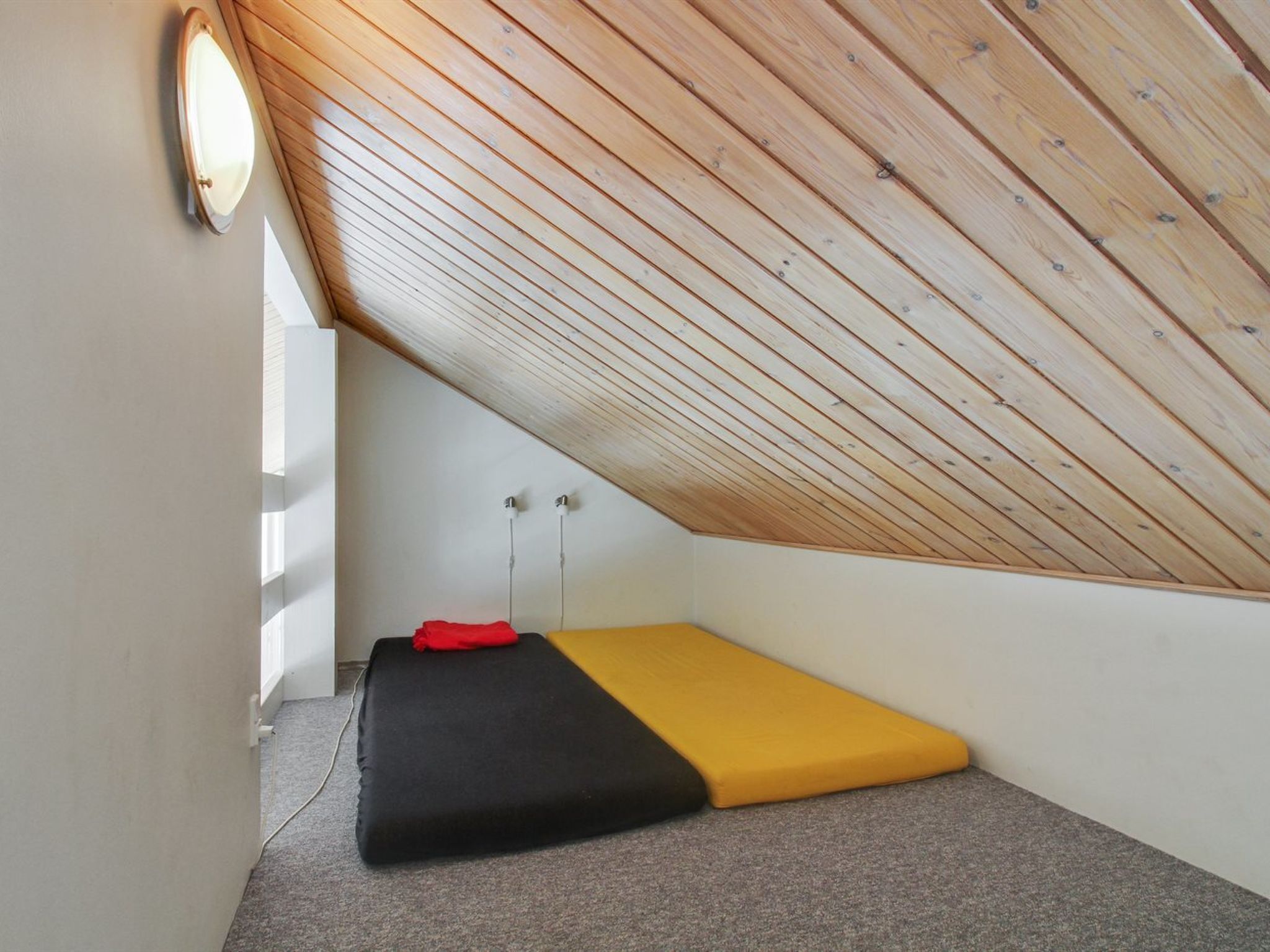 A small, sloped-roofed room with a simple bed and a small table.