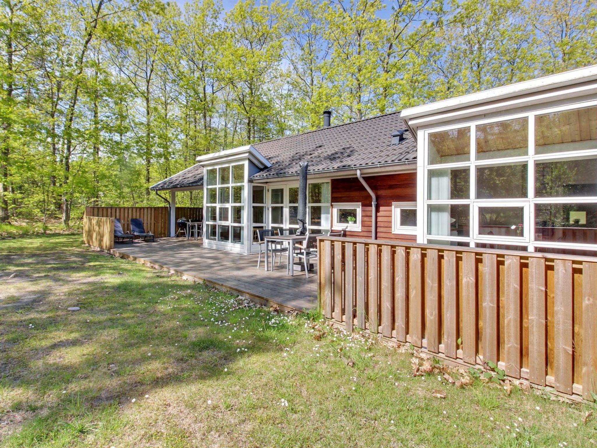 A wooden cabin with a deck, large windows, and a fenced yard.