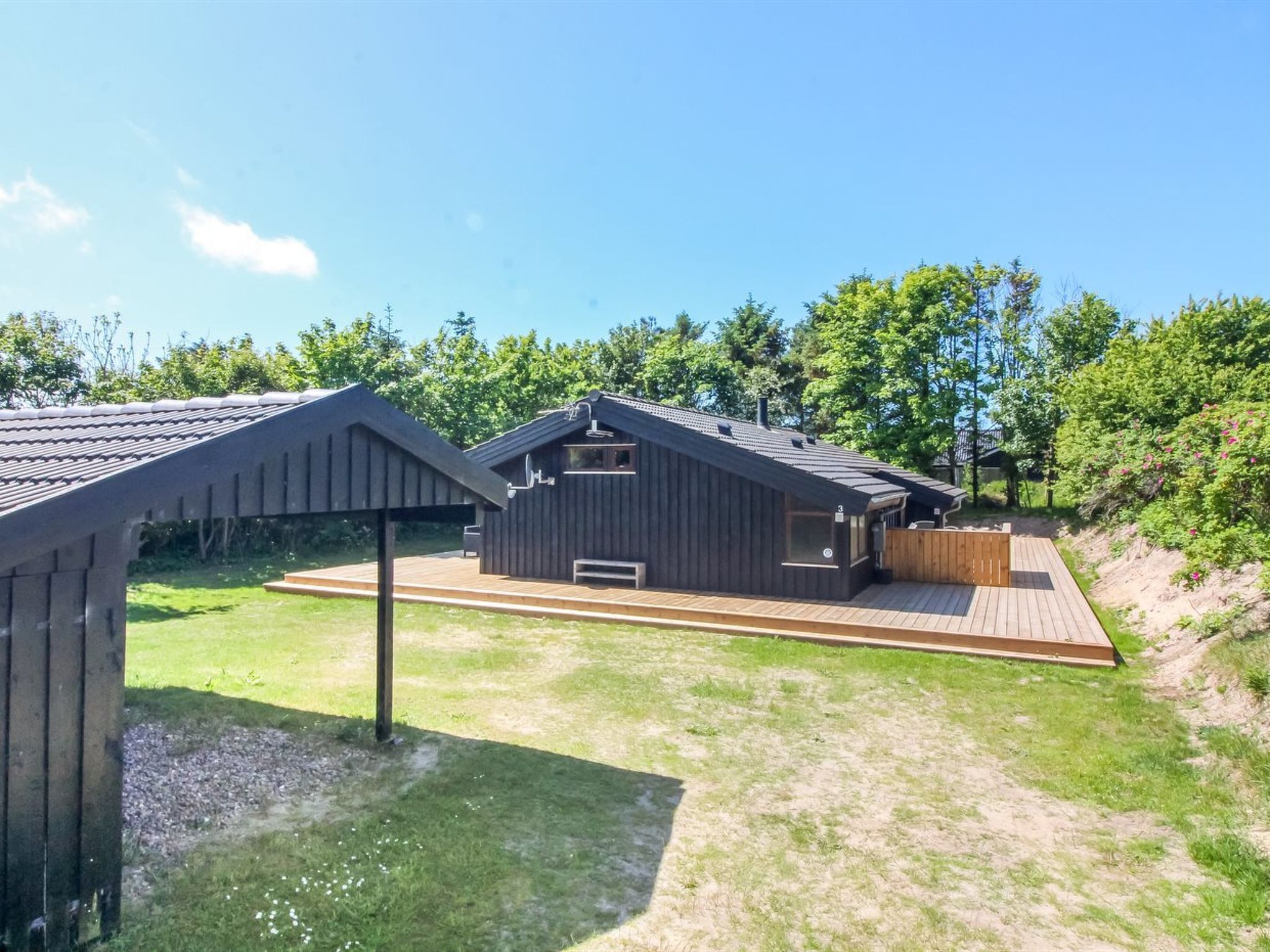 Een moderne cabin met een houten terras, een kleine buitenkeuken en een overdekte zithoek.