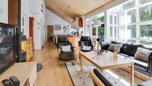 Amplia sala de estar con un alto techo de madera, una chimenea, un sofá, una mesa de centro y una cocina al fondo.