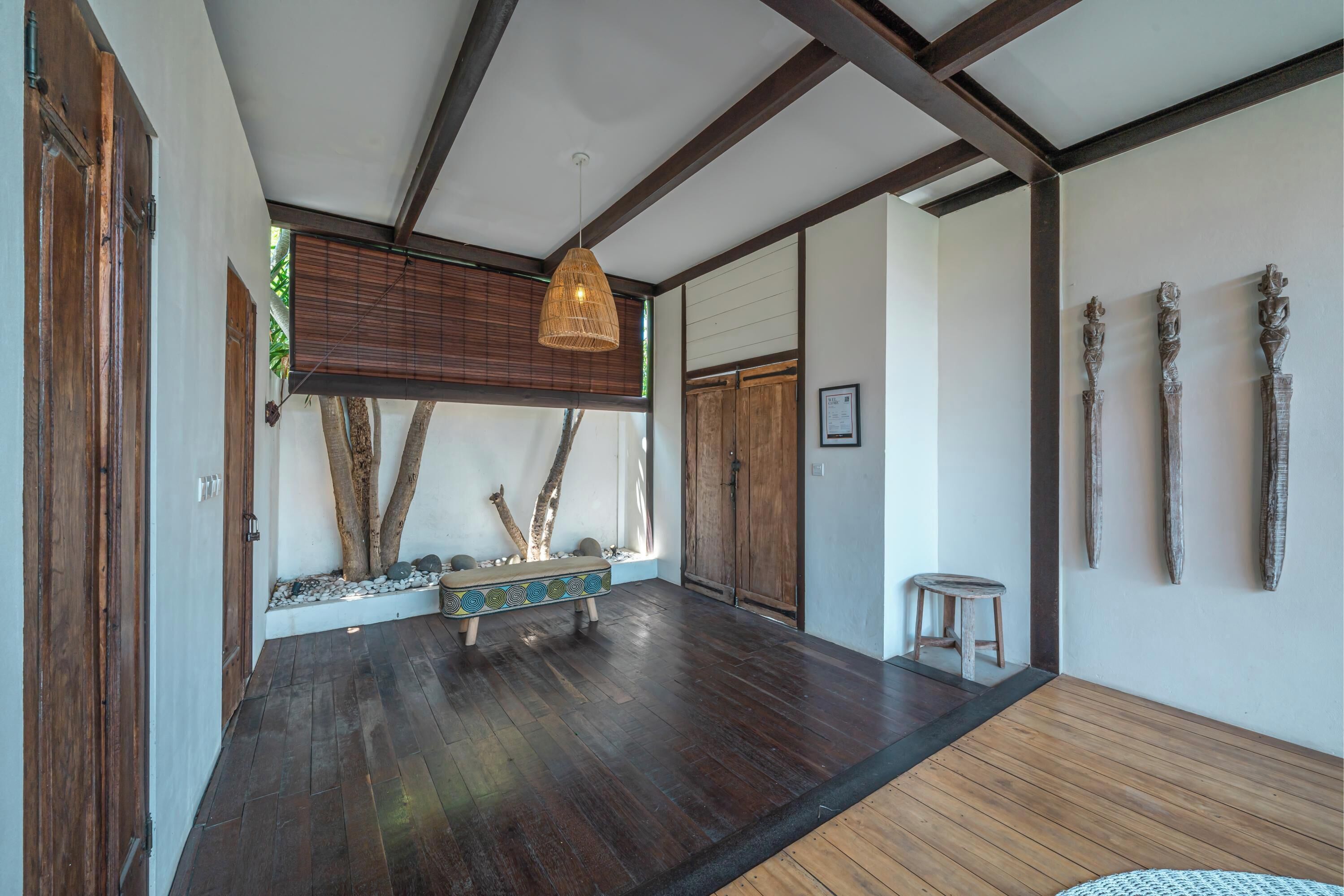 A spacious room with a wooden floor, a hanging light fixture, and a bench with decorative elements.