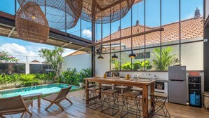 A spacious patio with a wooden table and chairs, a pool, and a kitchen area with a refrigerator and cabinets. - Villa Elma - 2BR pool villa in Umalas (Kerobokan)