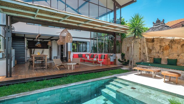 A modern outdoor pool area with a wooden deck, seating, and a stone wall. - Villa Elma - 2BR pool villa in Umalas (Kerobokan)