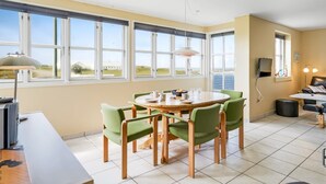 A dining area with a round table, green chairs, and a view of the outdoors through large windows. - "Ima" - 60m from the sea by Interhome (Løkken)