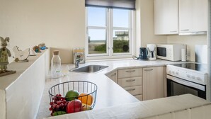 A modern kitchen with a large window, white cabinets, a sink, a coffee maker, a microwave, and a fruit bowl on the counter. - "Ima" - 60m from the sea by Interhome (Løkken)