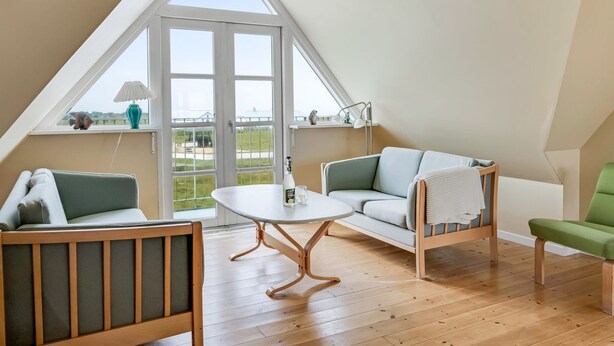 A cozy room with a sloped ceiling, wooden beams, a large window, and a seating area with a table. - "Ima" - 60m from the sea by Interhome (Løkken)