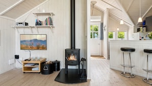 A cozy room with a wood-burning stove, a bookshelf, a flat-screen TV, and a kitchen area with bar stools. - "Dagmar" - 300m from the sea by Interhome (Hasle)