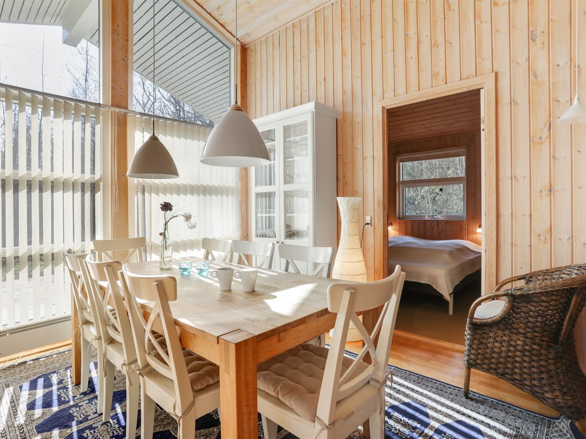 Accogliente interno di una baita di legno con zona pranzo, un letto e una poltrona in vimini.