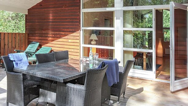 Un patio exterior con una mesa y sillas, una terraza de madera y un ventanal de vidrio que da a un espacio interior.