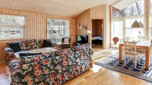 Interior acogedor de una cabaña con techo de madera, un sofá floral, una mesa de comedor con sillas y un televisor en una esquina.