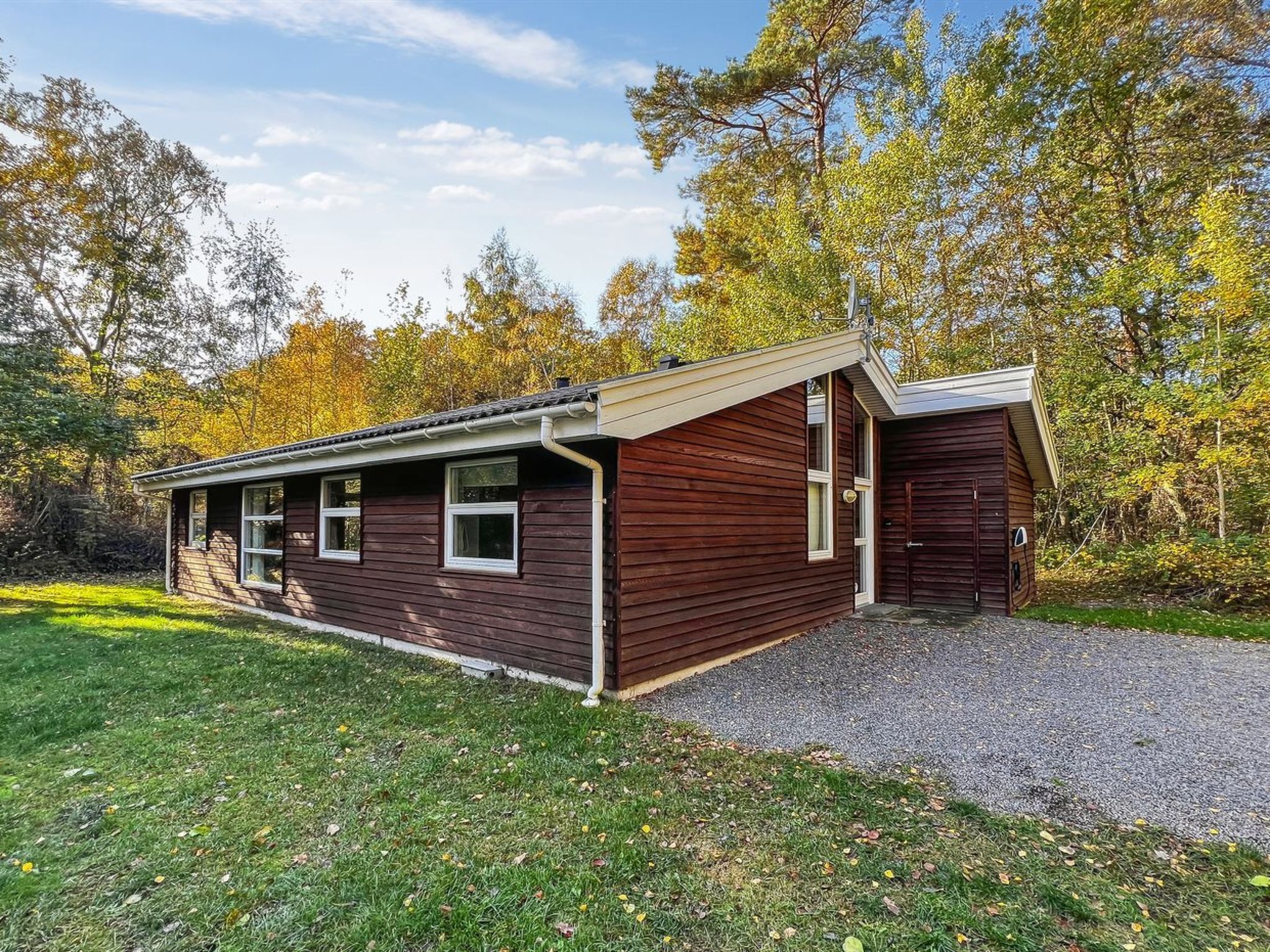 A wooden cabin with a sloped roof, a front porch, and a gravel driveway.
