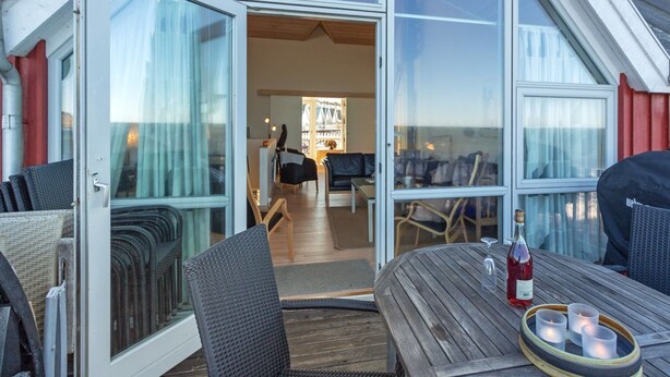 An open sliding glass door leading to a cozy interior with a dining area, a sofa, and a table with candles and a bottle. - "Halldora" - 10m from the sea by Interhome (Hasle)