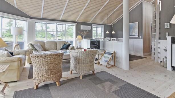 A spacious living area with a high ceiling, large windows, and a kitchen area.