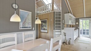 A dining area with a wooden table and chairs, a clock, and framed artwork on the wall.