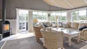 A cozy living room with a fireplace, wicker furniture, and large windows.